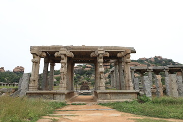 Fototapeta premium Ancient stone buildings in Hampi, Karnataka, India, surrounded by grasslands and granite boulders, reflecting the architectural heritage of the Vijayanagara Empire within the UNESCO World Heritage Sit