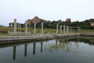 Obraz premium Ancient stone buildings in Hampi, Karnataka, India, surrounded by grasslands and granite boulders, reflecting the architectural heritage of the Vijayanagara Empire within the UNESCO World Heritage Sit