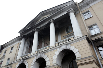 Naklejka premium Neoclassical building facade after a fire photographed from a low angle, showing tall columns, arched entrances, balustrade balcony and weathered plaster that conveys history, grandeur and urban decay