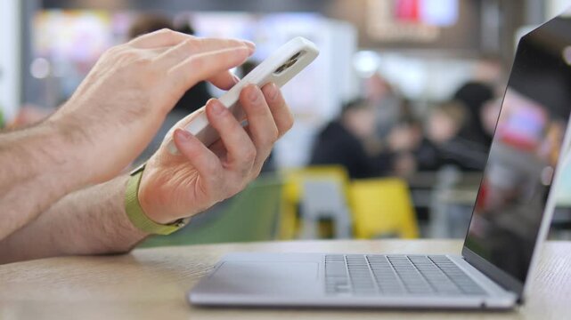 Hands multitask on phone and laptop in cafe. Person focused, calm, and engaged in digital work. Suitable for remote work, digital lifestyle, or tech-related content