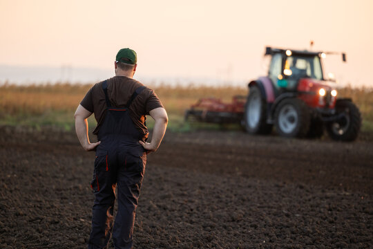 Farmer Looking at Tractor on Freshly Plowed Agricultural Field at Sunset