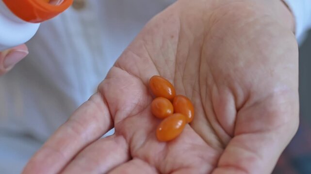 Close-up of orange pill capsules spilling from bottle into woman's palm. Taking vitamins, antioxidant coenzyme Q10, and dietary supplements. Health concepts and daily routines for health and beauty.