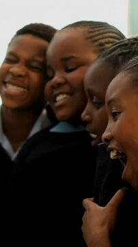 Vertical video: Smiling group of four students leaning in at school, hearing joke in uniforms