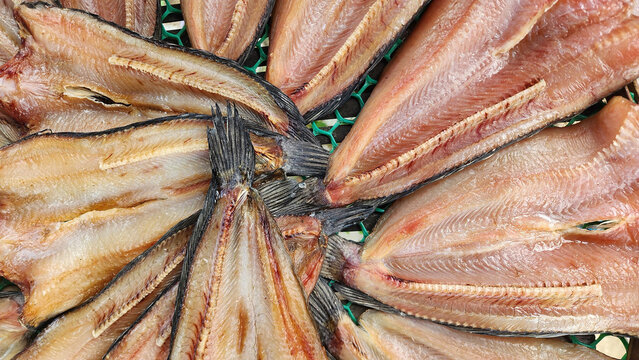 A top-down view of sun-dried striped snakehead fish split open and arranged in a circular pattern on a mesh tray at a traditional Thai market.