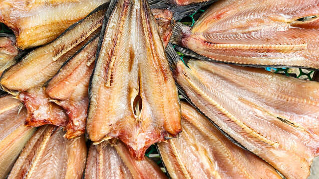 A top-down view of sun-dried striped snakehead fish split open and arranged in a circular pattern on a mesh tray at a traditional Thai market.