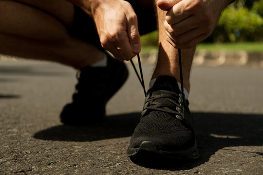 Person crouching to tighten laces on black athletic shoes during run