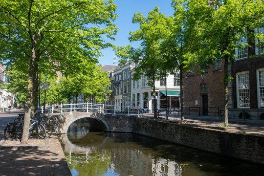 Historic canal houses and arched bridge in Delft City Centre on sunny spring day, Netherlands