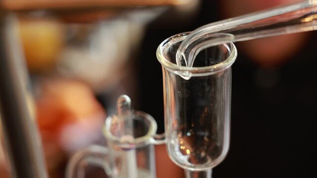 Gin distillation alcohol clear liquid pouring into glass vessel laboratory equipment close up transparent scientific process beverage production precise modern technique controlled environment