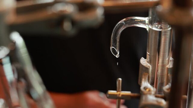 Distillation alcohol gin laboratory glass equipment liquid chemistry science process closeup transparent tube apparatus metal clamp clear liquid precise experiment industrial production beverage