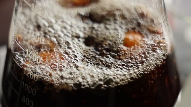 Macro closeup of carbonated dark soda with bubbles, fizzy beverage refreshment, drink texture and lively surface, ice in glass beaker, summer drink and science chemistry concept