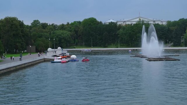 Pedal boat moving on a pond in a summer park with a fountain in the middle. Tourists enjoying leisure water activity during a sunny day at the city park.
