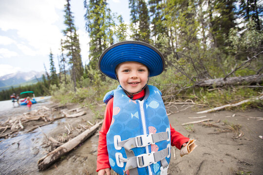 Happy young boy in a life vest eating a snack by the river