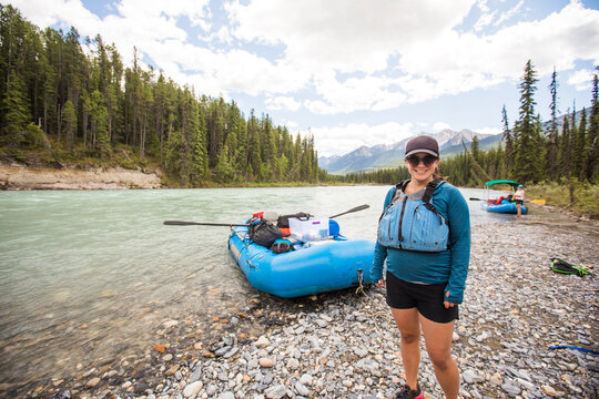 Happy woman stands by a raft on a rocky riverbank
