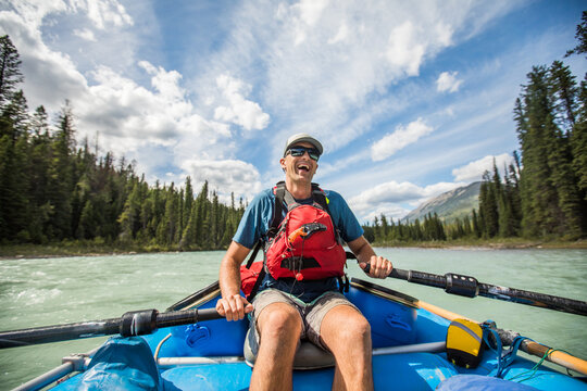 Laughing man rowing a raft on a scenic river