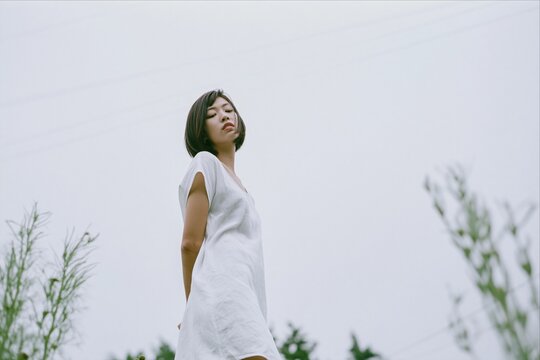 Young Asian woman in white dress under an overcast sky