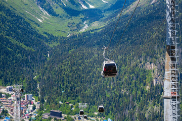 Aerial perspective of gondola lifts carrying passengers above vibrant green mountains and a quaint town nestled in the valley below © Anat art