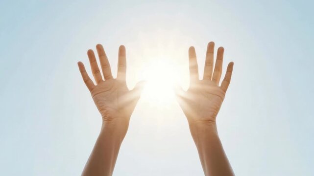 Pair of human hands raised toward bright sunlight in clear blue sky expressing hope, faith, spirituality, energy, and connection with nature and universe