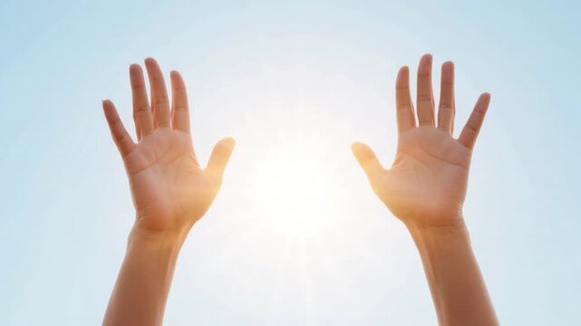 Two raised human hands reaching up toward bright sunlight in clear blue sky symbolizing hope aspiration freedom and spiritual connection with nature