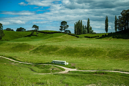 The scene shows lush green hills with large farm bales arranged near a dirt path