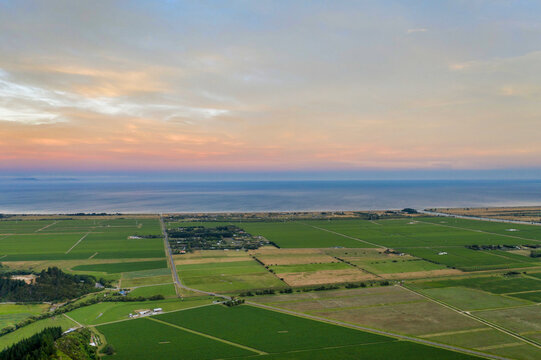 Aerial view of expansive farmland stretching toward the ocean under a soft pastel sky
