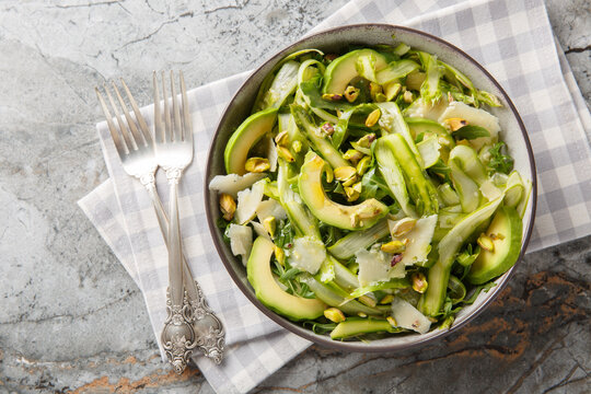 Freshly mixed greens salad with shaved asparagus, parmesan, pistachios, avocado and arugula closeup in the plate on the table. Horizontal top view from above