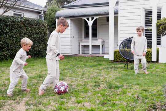 Young boy ready to kick a soccer ball to his brother while other brother looks on
