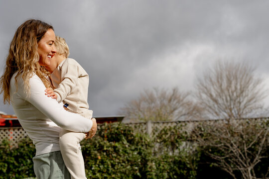Mother carrying preschooler in a backyard with grey clouds in the background