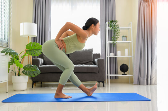 Young woman practicing standing balance yoga pose on exercise mat in modern living room at home for strength, flexibility and healthy lifestyle
