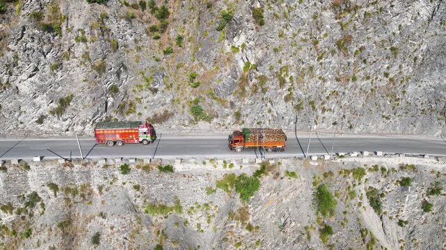 Drone shot of commercial lorries navigating a steep cliff road in India.