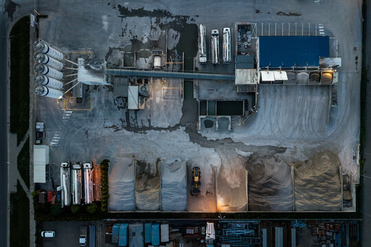 Aerial view of a cement production facility featuring storage silos, industrial trucks, and piles of raw materials in an industrial zone in Warsaw, Masovian Voivodeship, Poland.