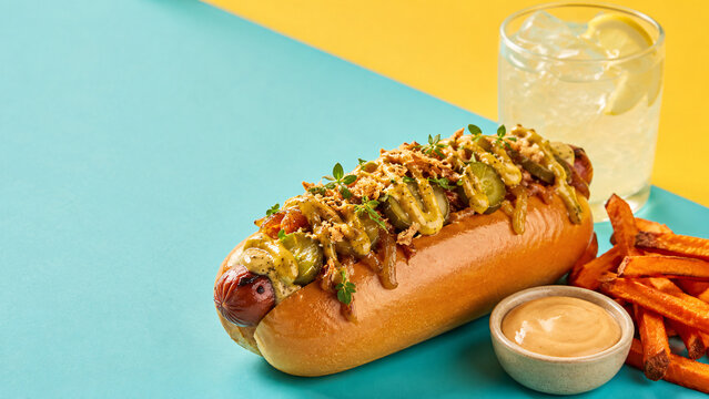 Hot dog gourmet z batatowymi frytkami i lemoniadą na kolorowym tle