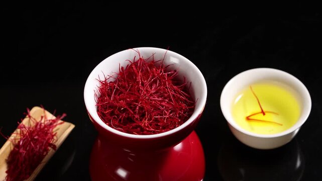 High-angle close-up of premium dried saffron threads in a ceramic bowl with saffron tea infusion on a black background