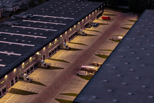 Aerial view of a logistics center at night with illuminated loading docks, warehouse buildings, and a parked truck in Warsaw, Masovian Voivodeship, Poland.