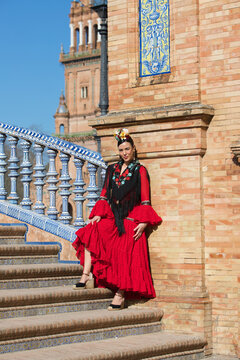 A beautiful woman dancing flamenco in a square in Seville, Spain. She is wearing a red ruffled dress and a flower in her hair, posing for the photo. Flamenco, a UNESCO Intangible Cultural Heritage.