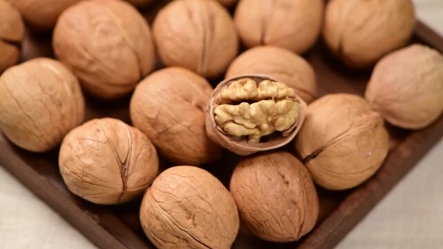 Top view of fresh whole walnuts and walnut kernels arranged on a rustic wooden tray, macro shot with soft lighting