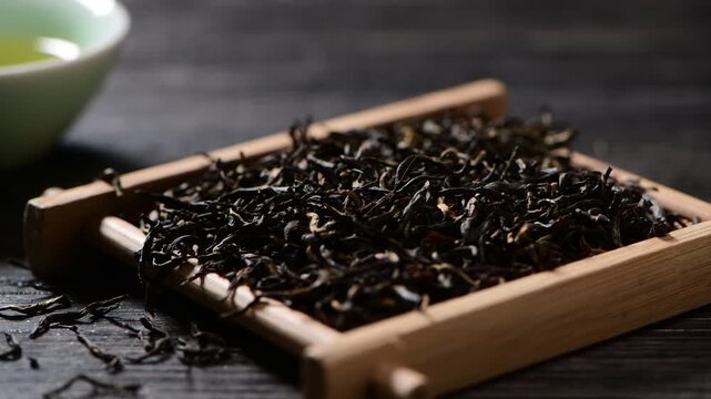 Close-up of high-quality dried black tea leaves on a small wooden tray, traditional tea ceremony preparation, dark rustic table setting