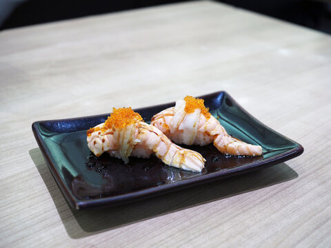 Salmon Sushi Nigiri grilled or aburi topped with engawa and salmon roe served on black plate.
