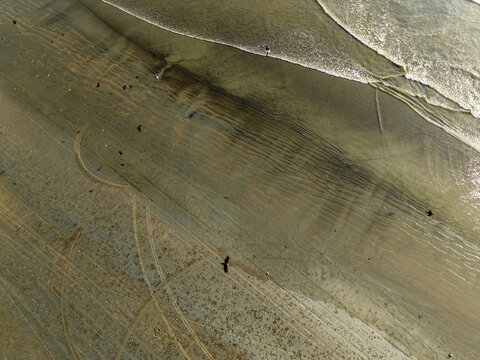 Aerial view of Sea-View Beach with wet sand, tire tracks, and birds flying over the shoreline in Karachi, Sindh, Pakistan.