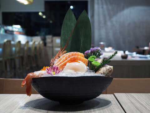 Ceramic bowl of fresh sliced salmon, ebi or shrimp and hotate sashimi served with seaweed, wasabi and marigold flower over ice. J