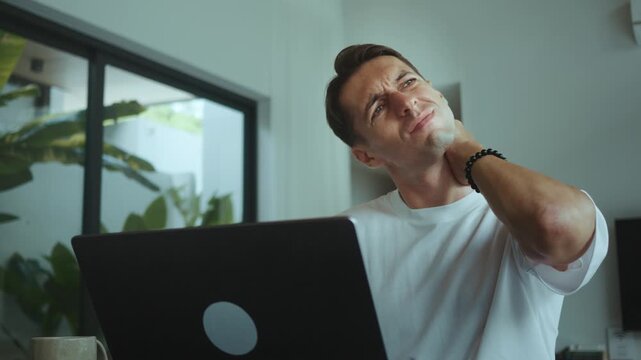 Millennial business man working on laptop touching neck feeling pain discomfort and stress remote work problem health issue office lifestyle tired businessman experiencing strain at home workspace