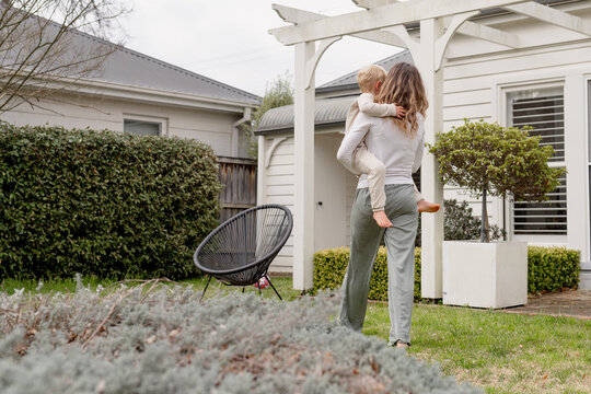 Mother walking away carrying son in their backyard