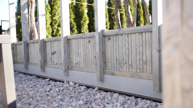 Low angle pans trace wood base panels, posts, and slats on crushed stone as camera moves left to right. Shallow depth highlights grain, joints, screws, and glass edges.