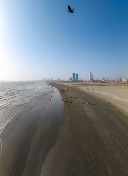 Aerial view of Sea-View Beach with people walking on the sand, gentle waves, and the modern skyline of Karachi in the distance, Karachi, Sindh, Pakistan.