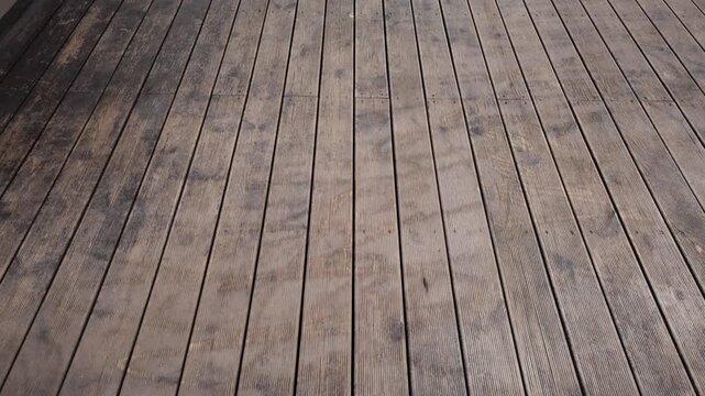Parallel grooved wooden planks show screw lines, narrow gaps, and patchy dark stains in daylight as the camera pans slowly, with even lighting and shallow depth.