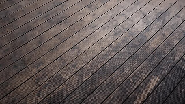 Weathered Grooved Wooden Deck Planks With Diagonal Alignment. Grooves, screw heads, and repair patches are visible, late afternoon light, soft pan and high contrast.