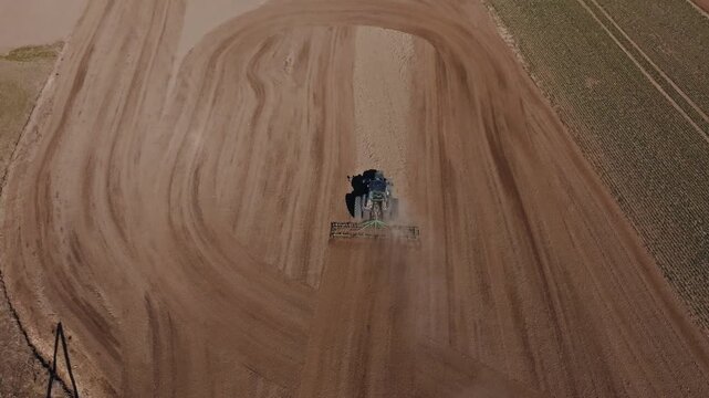 Title Aerial tractor with harrow carves curved tracks on plowed field. Operator sits centered, dust plume moves, tire ruts repeat, crop strip and tramlines align, daylight top down view.