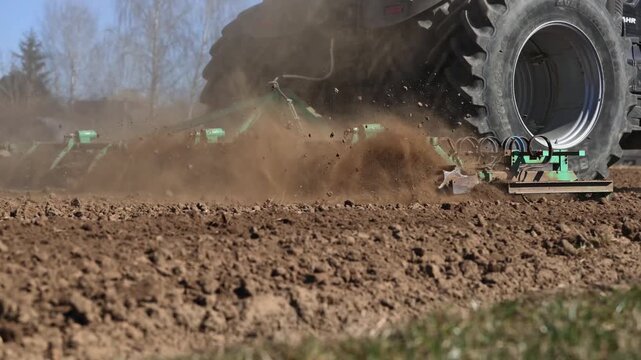 Low angle view of Deutz Fahr tractor with multi disc cultivator in motion. Title in description. Tines churn soil, dust flies, dual tires and rotating discs show power.