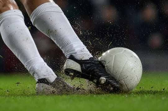 激しくボールを蹴るサッカー選手の足元クローズアップ、芝生と飛び散る泥のダイナミックな瞬間