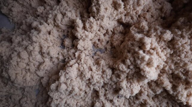 Close up loose tan fiber mounds, slow pan reveals texture and form. Camera pans left to right, material inspection of loose fill insulation or cellulose