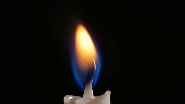 Macro view of burning candle wick with blue base and yellow orange flame glowing in dark